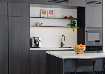 Moderne keuken met kookeiland, donkere kasten en open nis met verlichting.