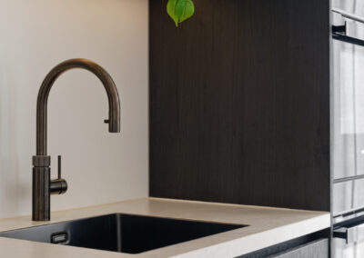 Moderne keuken met zwarte spoelbak, kraan en donkere achterwand.