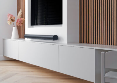 Strakke tv-wand met wit meubel, zwarte tv en houten lattenwand.