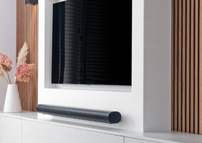 Strakke tv-wand met wit meubel, zwarte tv en houten lattenwand.