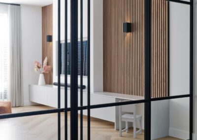 Glazen scheidingswand met zwart stalen frame en houten lattenwand.
