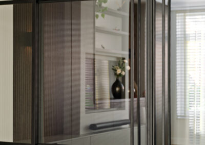 Doorkijk met glazen wand en zicht op houten kast met decoratie.