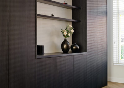 Donkere houten kastenwand met open planken en decoratieve accessoires.