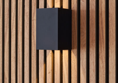 Zwarte wandlamp op houten lattenwand met modern design.