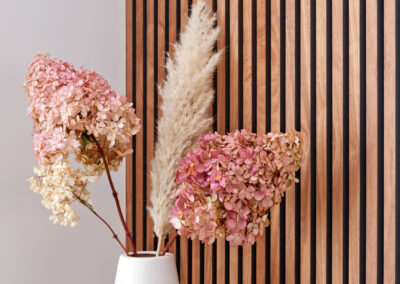Decoratieve wand met houten latten en vaas met droogbloemen.