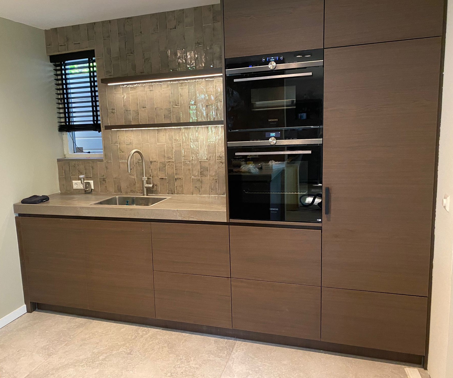 Wandkeuken met inbouwapparatuur Strakke wandkeuken met houten kasten, dubbele oven en geïntegreerde spoelbak.